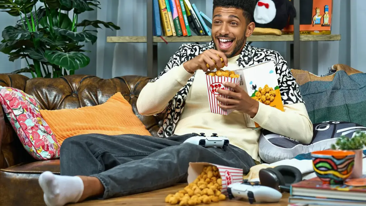 A bowl of plain air-popped popcorn sitting on a couch next to an attentive dog