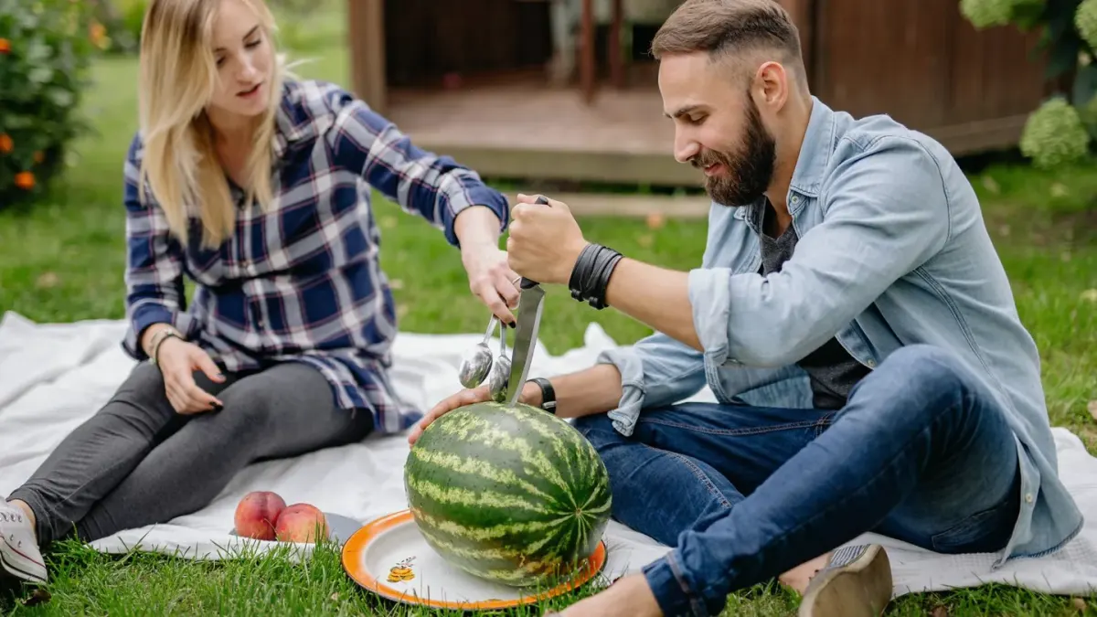 A dog investigating a cut slice of watermelon resting on a picnic blanket