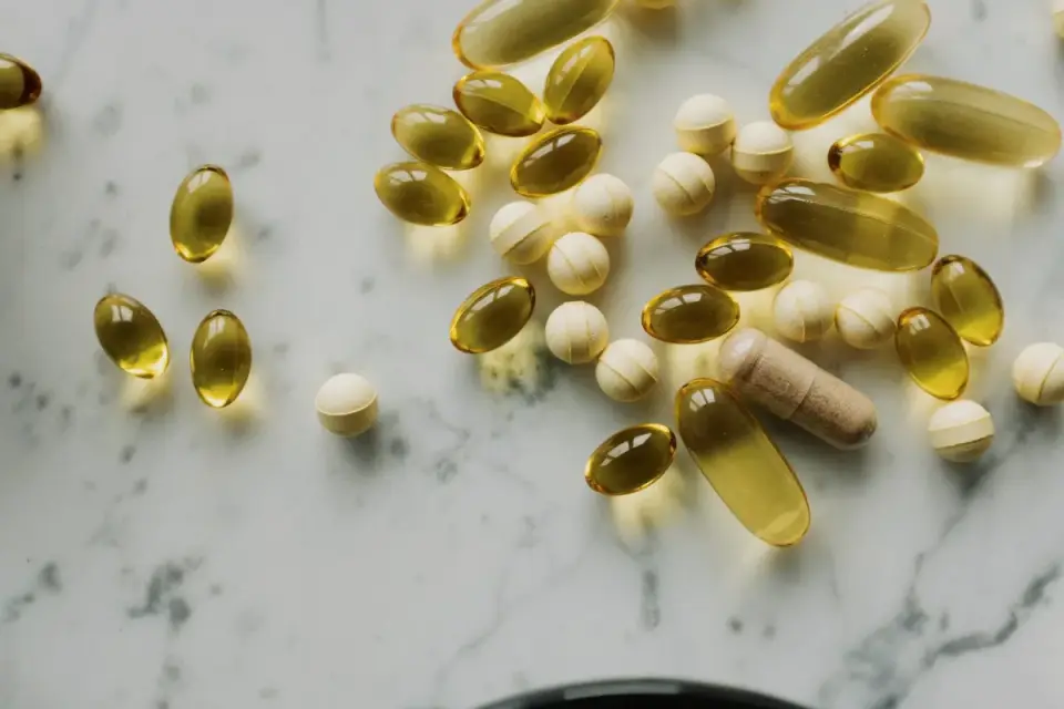 Fish oil softgel capsules next to a portion of raw salmon on a wooden surface