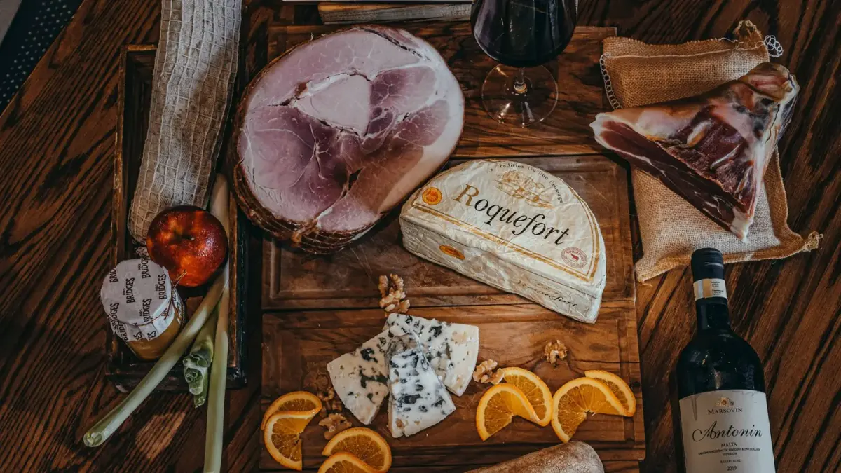 Slices of cooked ham on a wooden cutting board with a dog looking on from a distance